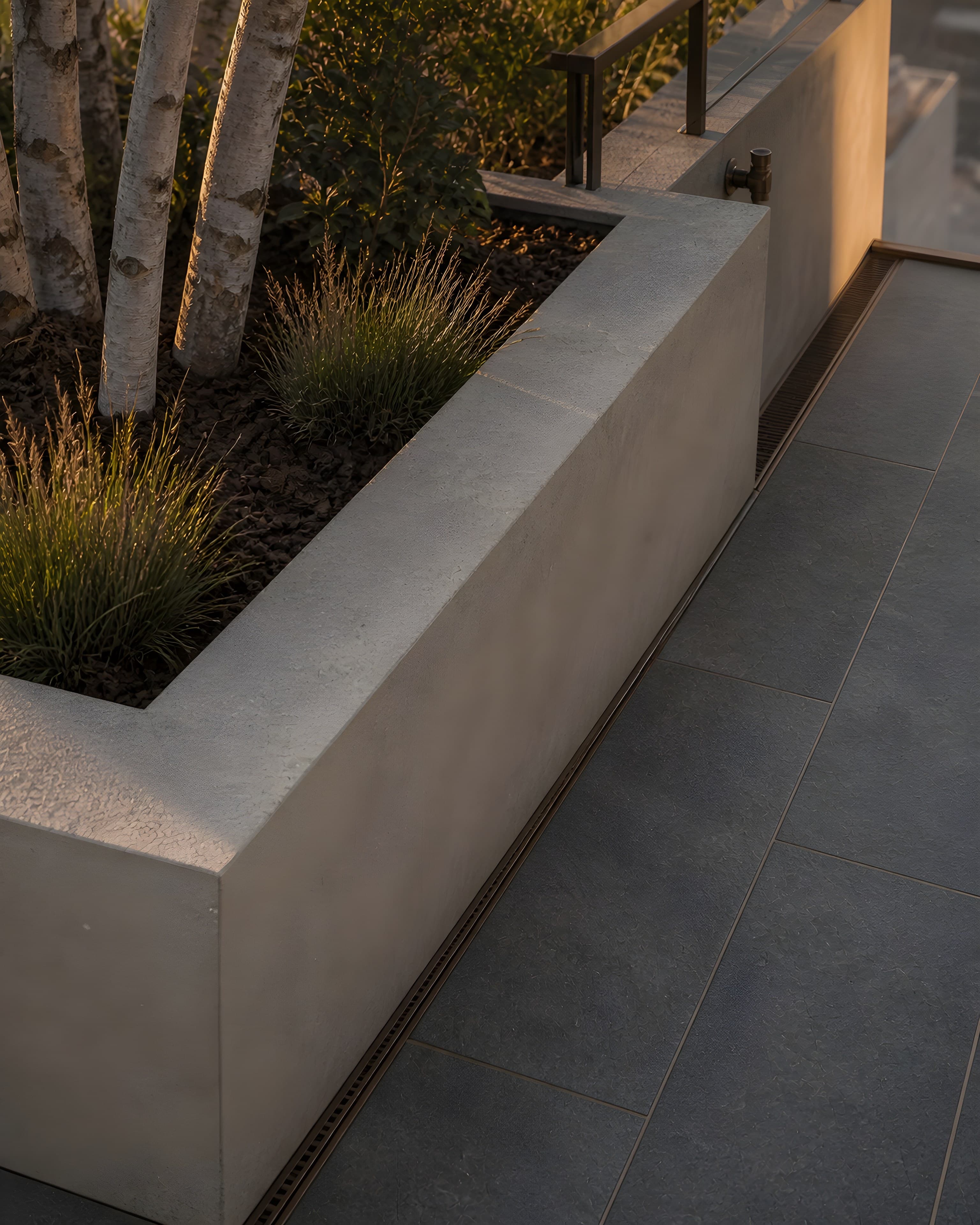 Close detail of an integral limestone planter with an eighteen-inch wall, deep soil beneath bark mulch, a bronze channel drain in the bluestone paving, and a bronze irrigation bib