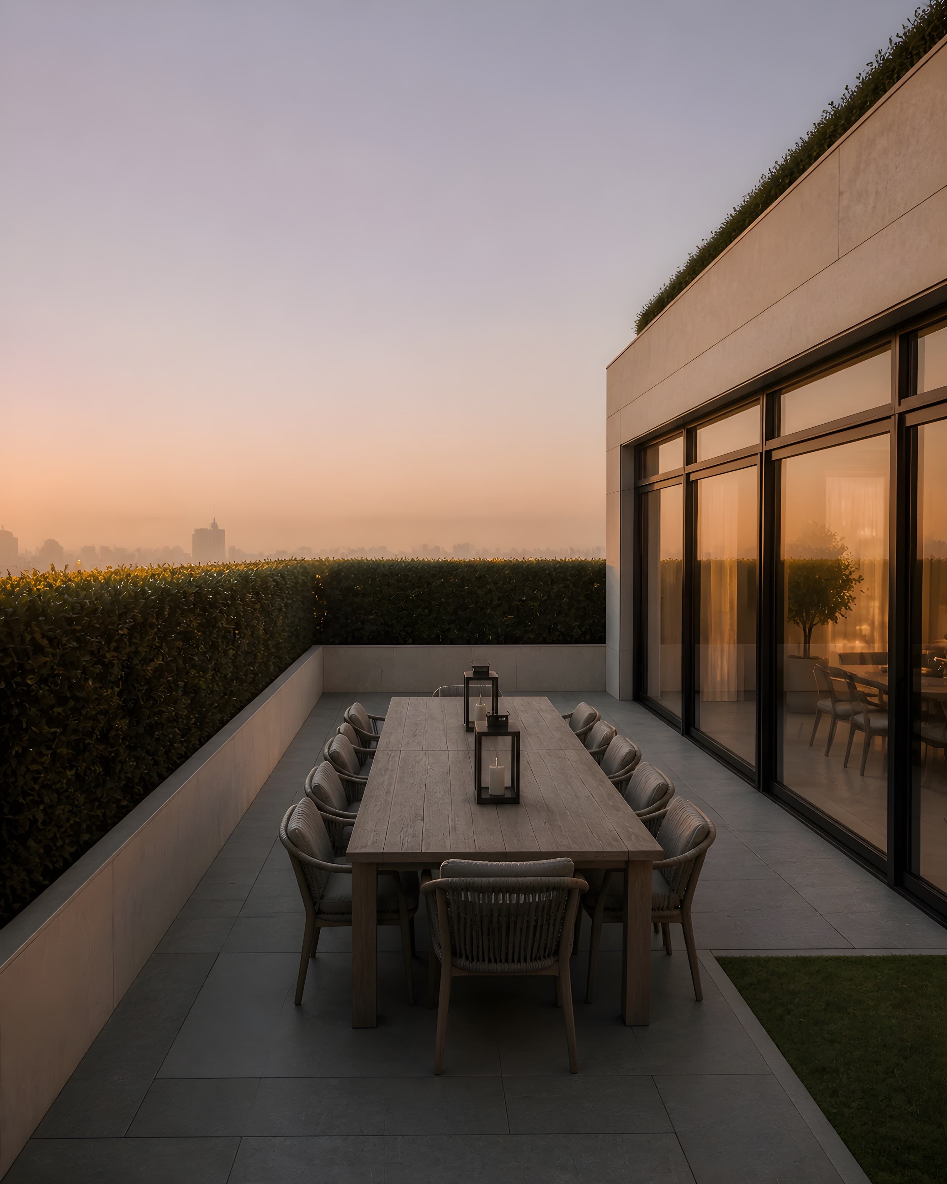 The dining zone at the east end of the terrace, a teak table for ten enclosed by shoulder-height hornbeam hedging, warm light inside the glazing behind