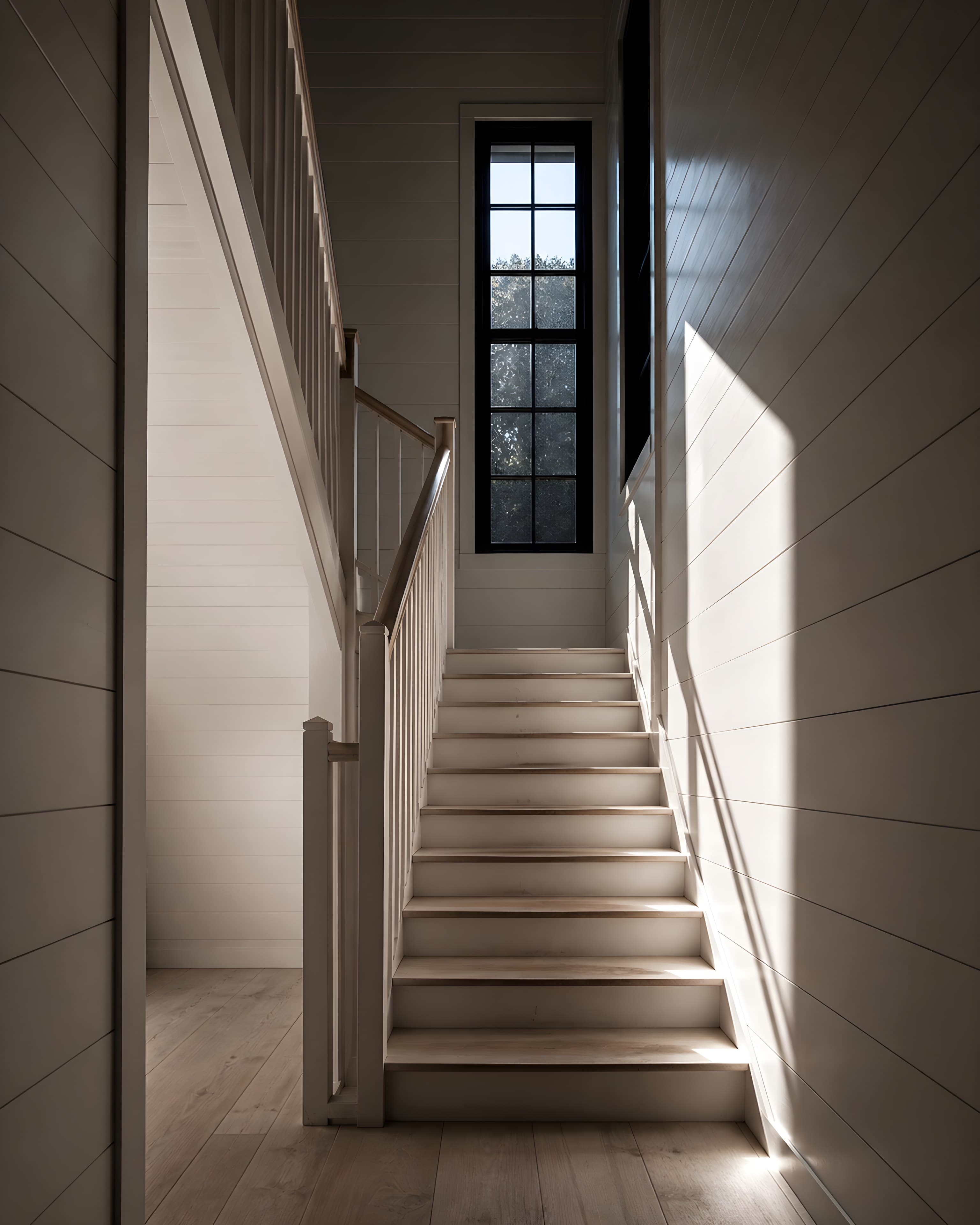 The main stair from below, painted balustrade and worn oak treads under a hard rectangle of light from the half-landing window