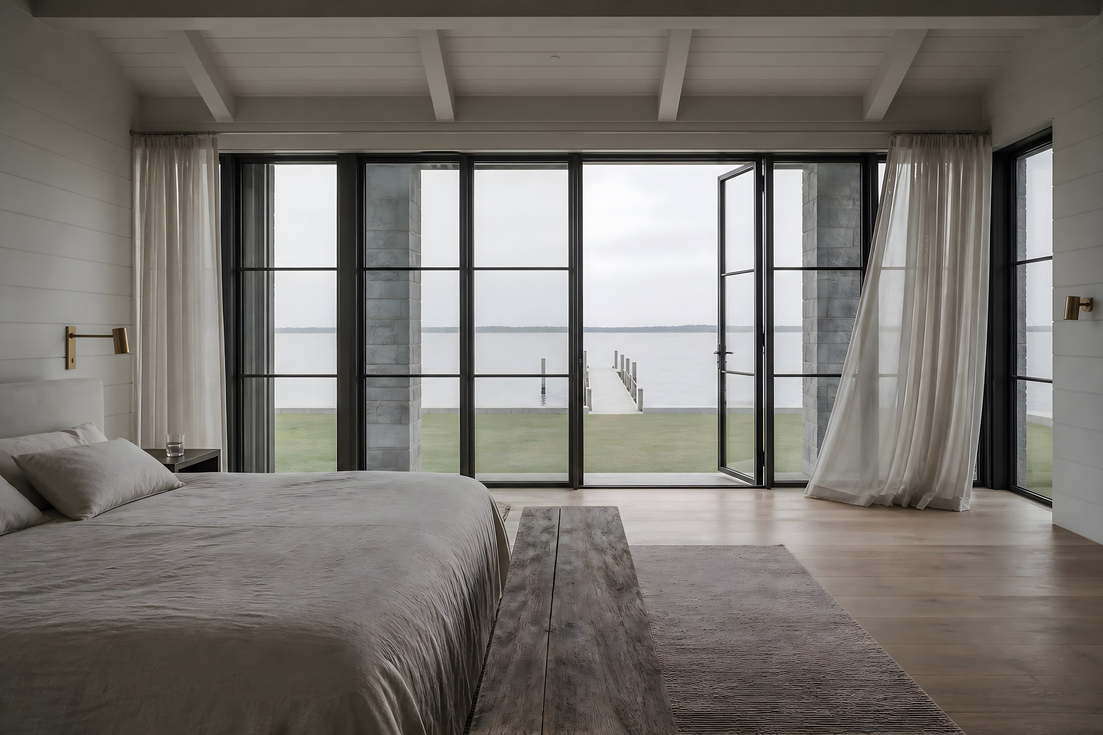 The primary bedroom at dawn in the upper glazed bay, a low linen bed facing a wall of casements onto a flat silver bay